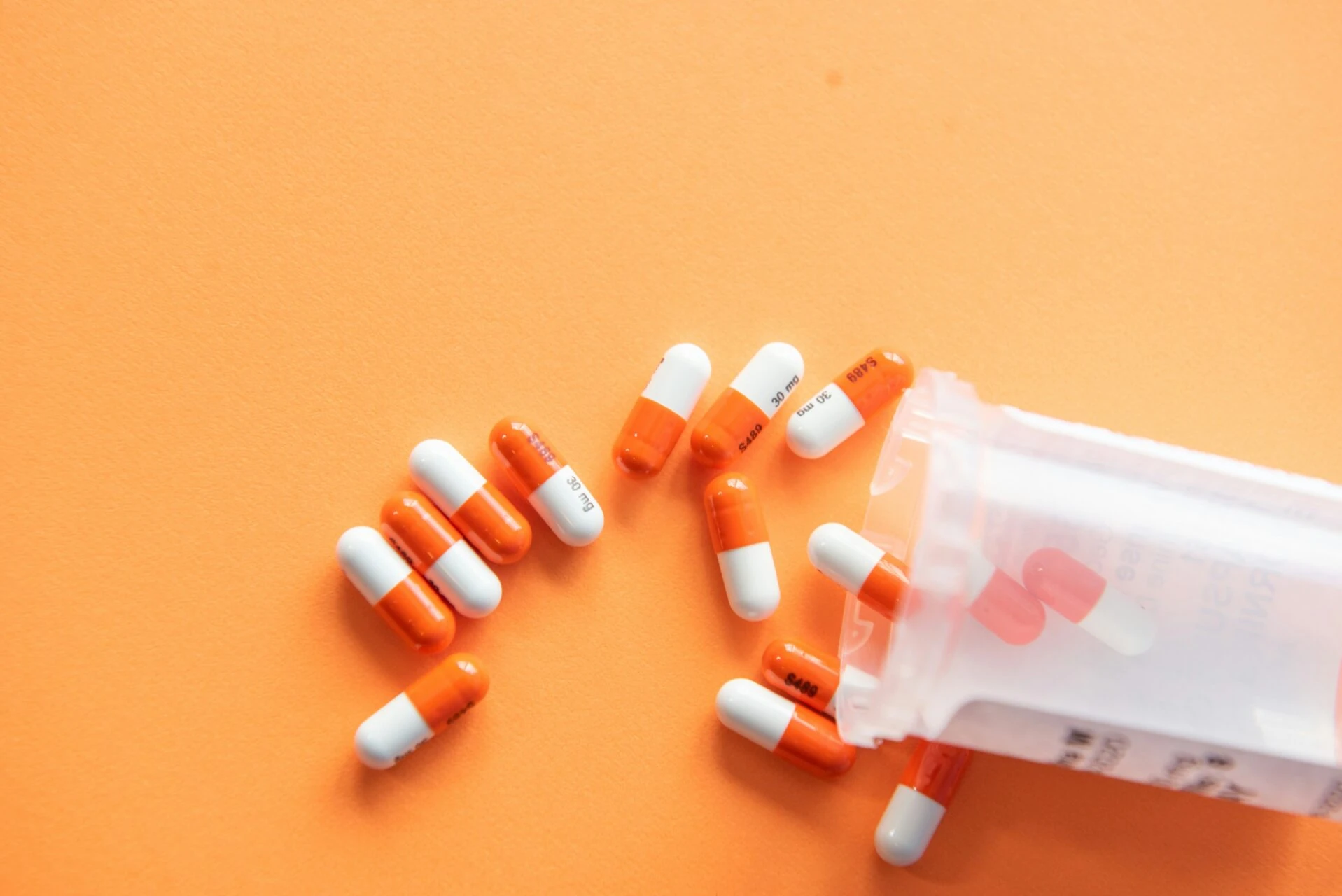 Prescription capsules spilling from a pill bottle on an orange background